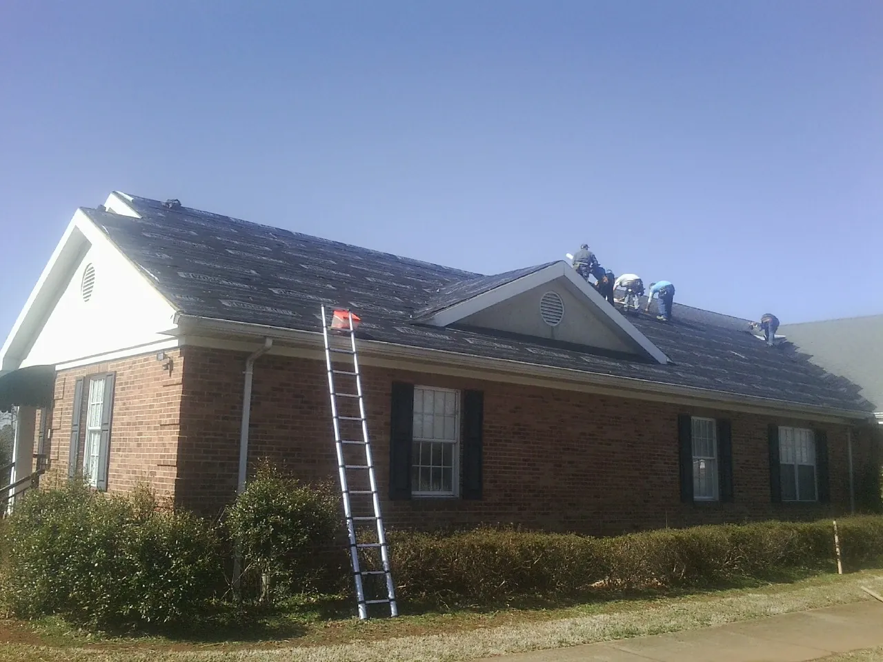 Crew tearing shingles off a brick ranch roof with a ladder set — Metal Roof Repair work by our crew in Union